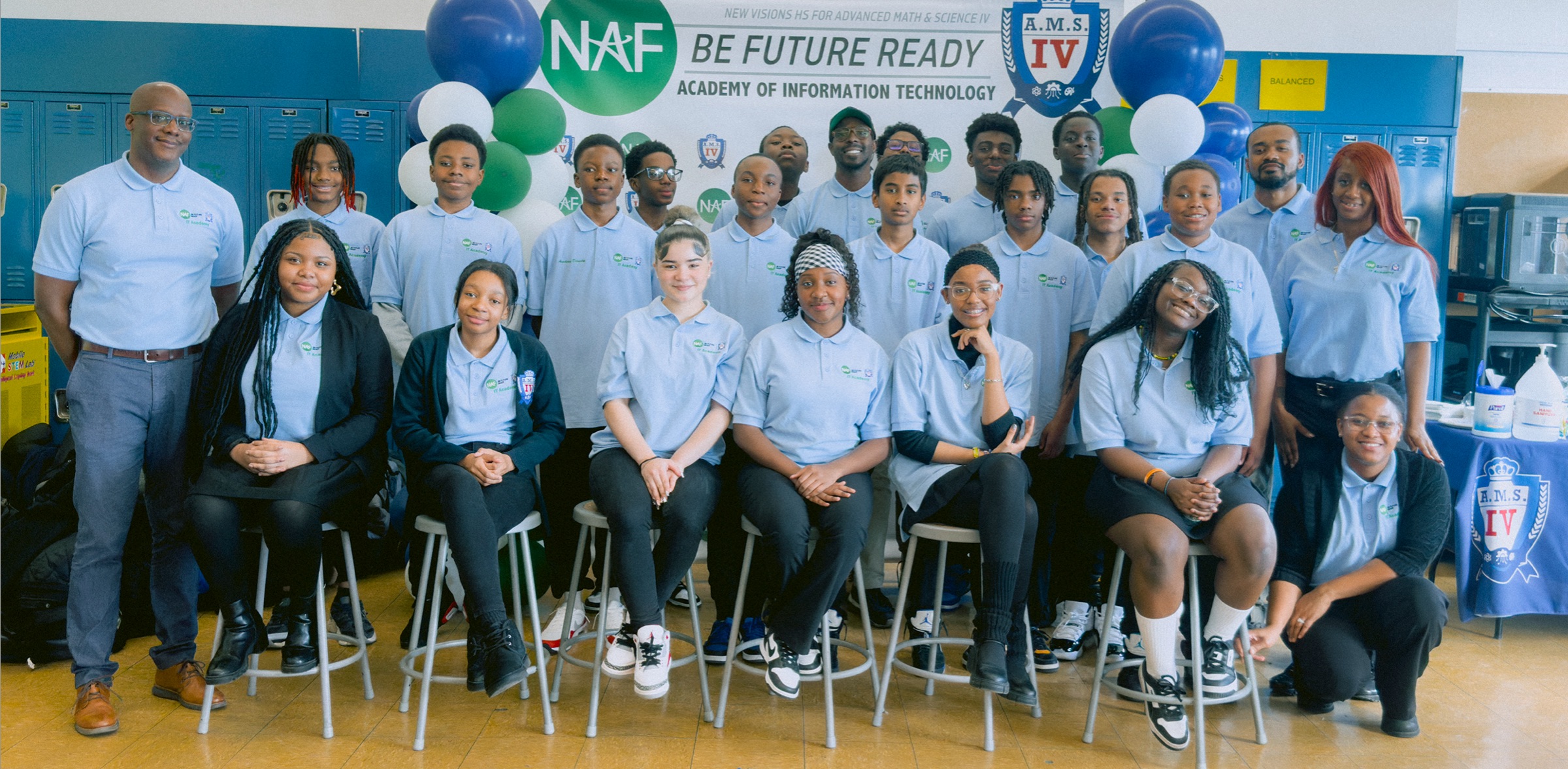 A group of students and teachers pose for a photo in uniform in front of a banner reading "Be Future Ready, Academy of Information Technology.