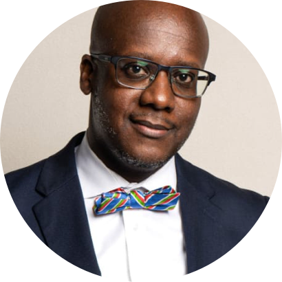 A man with glasses, wearing a dark suit, white shirt, and a colorful bow tie, poses for a professional headshot against a neutral background.