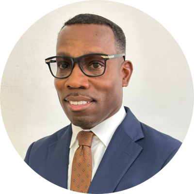 Man in a suit and tie wearing glasses, standing against a plain white background.