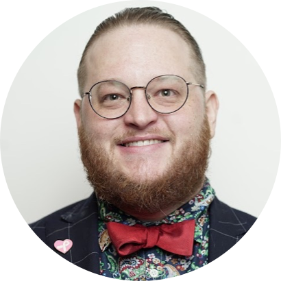 A person with glasses and a beard, wearing a red bow tie, a dark jacket with pinstripes, and a colorful, patterned shirt.