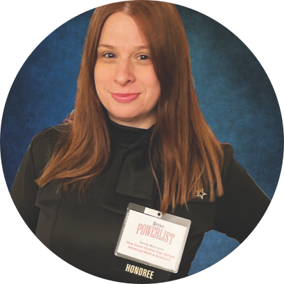 A woman with long red hair is wearing a black top and a name badge labeled "Bronx Powerlist Honoree" against a blue background.