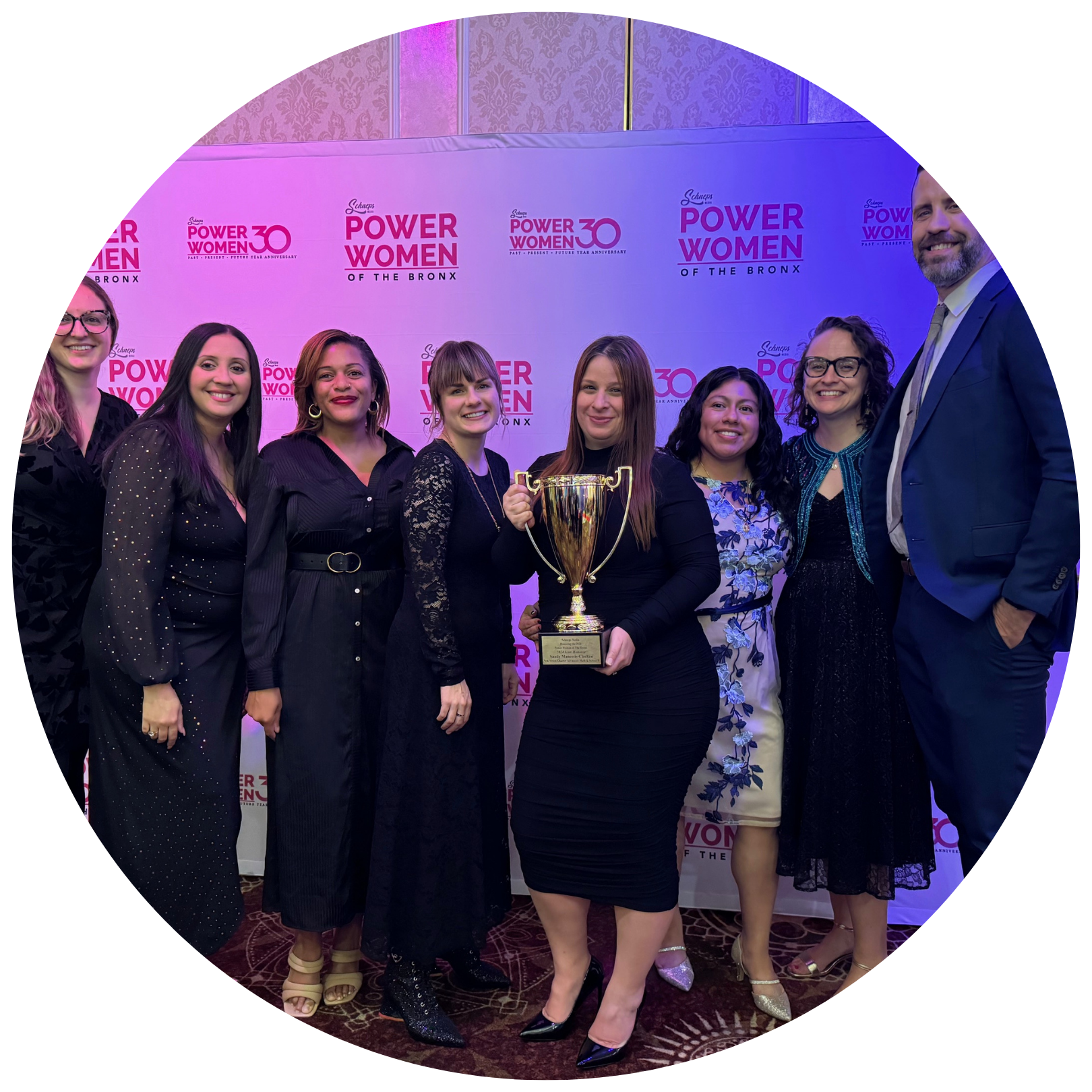 A group of people stands together, with one person holding a trophy, in front of a banner reading "Power Women of the Bronx.