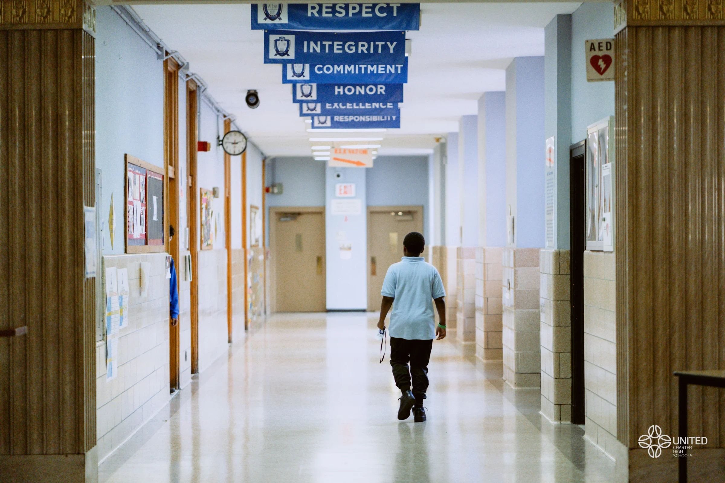 A student walks alone down a hallway lined with blue banners displaying values like respect, integrity, and responsibility.