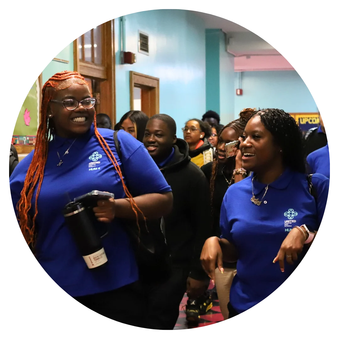 Two people wearing blue shirts walk down a hallway smiling, surrounded by others.