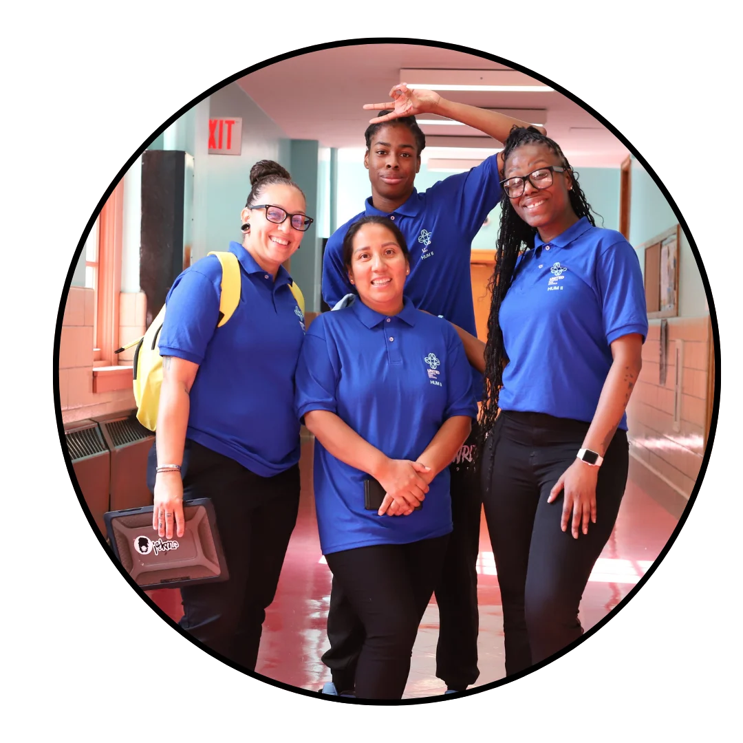 Four people wearing blue polo shirts pose together in a hallway, smiling towards the camera.