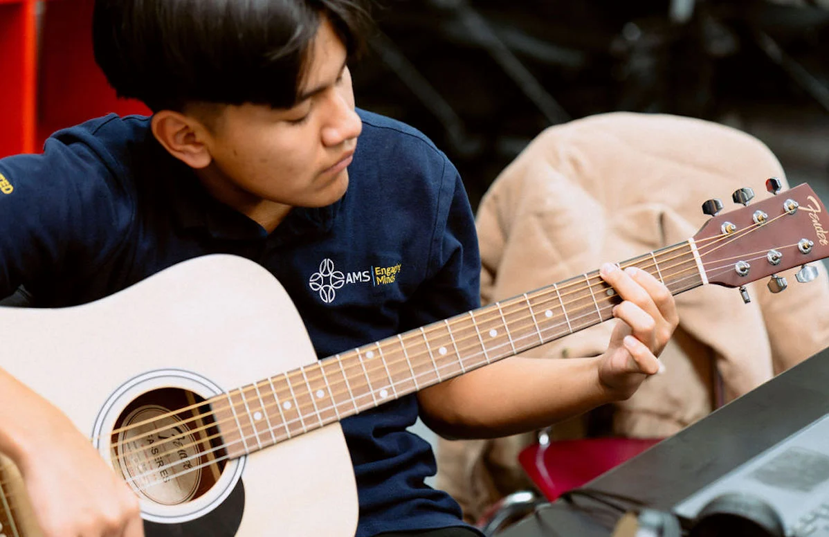 A student at United Charter High Schools practices playing a guitar. He's wearing a dark polo shirt.