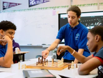 A teacher at United Charter High Schools stands in front of a digital whiteboard. There are students and desks in the foreground of the picture.