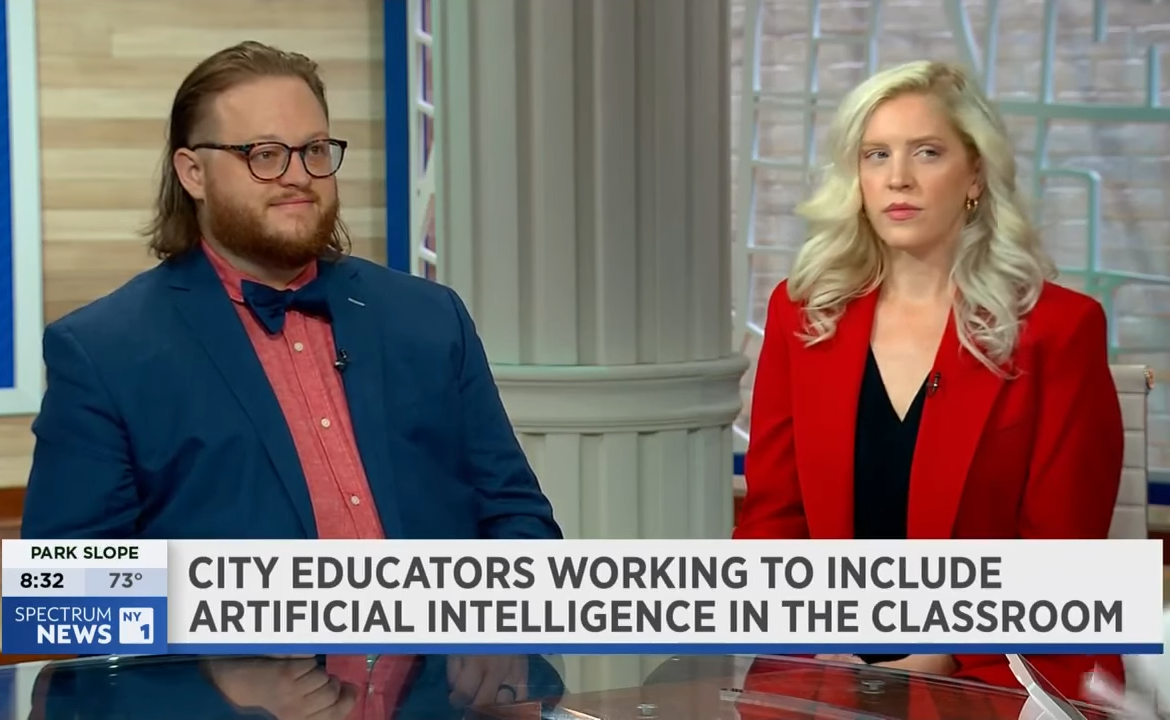 Two people in business attire sit at a news desk with a headline reading, "City educators working to include artificial intelligence in the classroom.