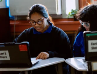 Two students at United Charter High Schools work together at desks. There are laptop computers on the desks.