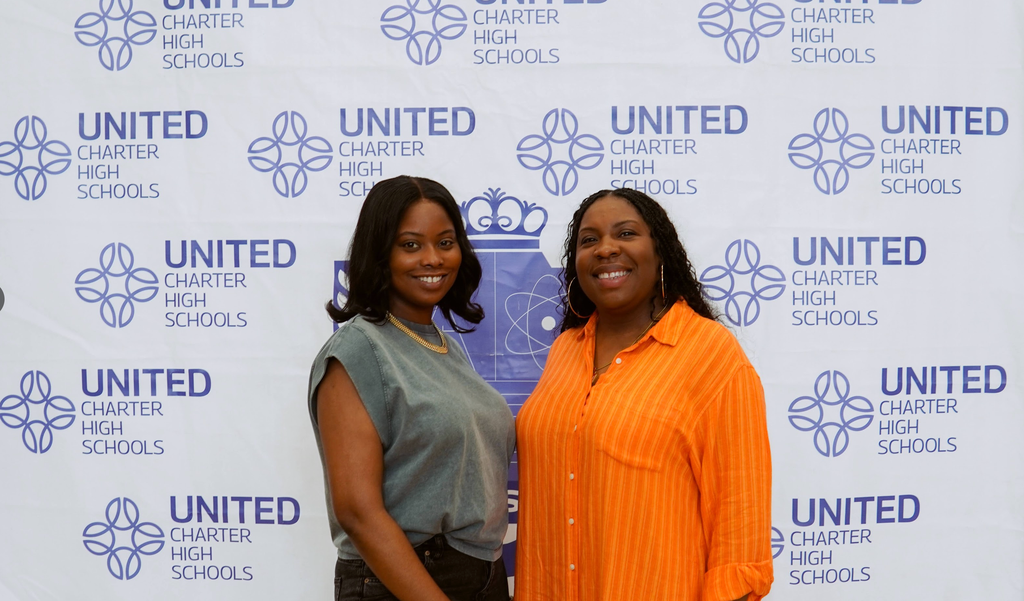 Two women stand smiling in front of a step-and-repeat banner with the "United Charter High Schools" logo.