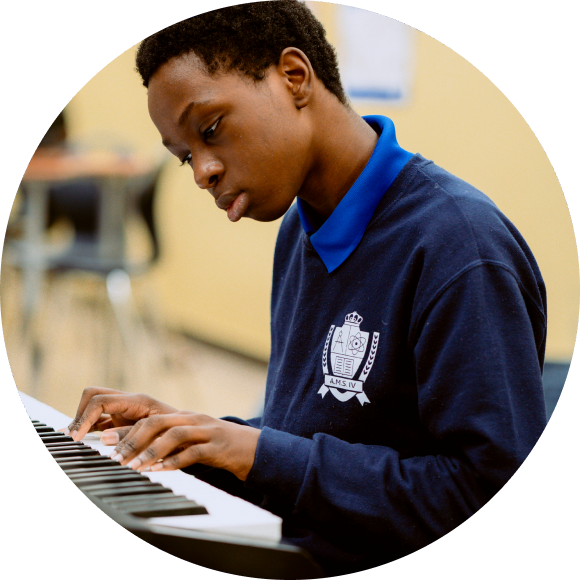 A student in a navy blue school uniform plays a keyboard in a classroom setting.