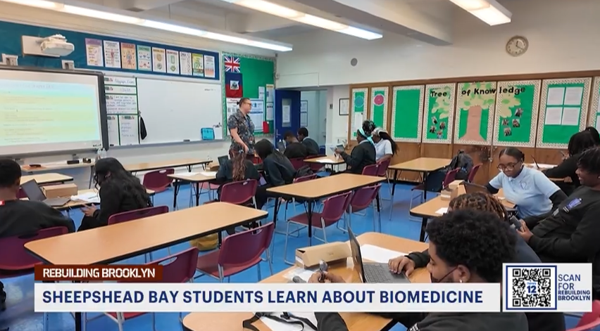 Students in a classroom work in groups and on computers while a teacher stands at the front; bulletin boards display the theme "Tree of Knowledge.