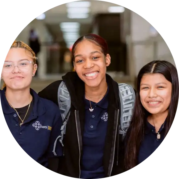 Three students in school uniforms smile and pose together in a hallway.