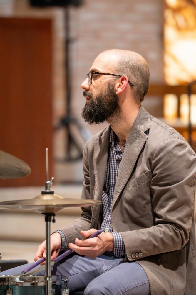 Michael Alfieri, music educator at United Charter High Schools Advanced Math & Science sits at a drum kit with drum sticks in hand